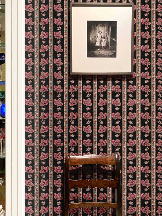 An interior wall with black floral striped wallpaper with a wooden chair in front