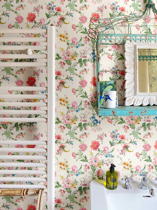 A floral wallpaper bursting with flowers in pinks, blues and yellows on a white background giving a vintage, granny vibe to bathroom walls