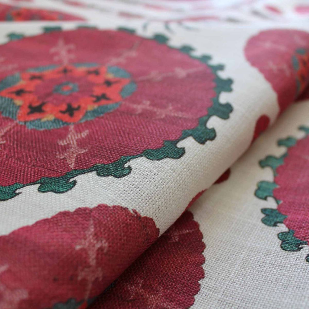Close-up of Paris Suzani fabric showcasing large traditional suzani floral motifs in dark pink and teal on an off-white background.